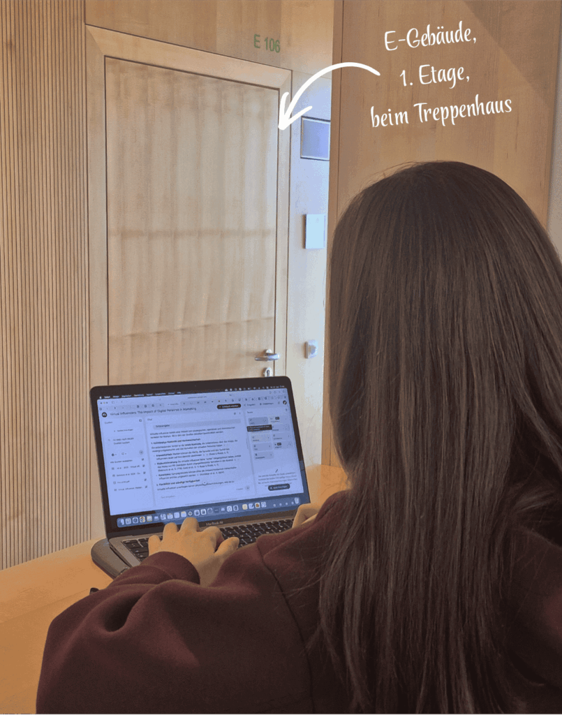 Marlene arbeitet am Laptop im E-Gebäude beim Treppenhaus in der Nische